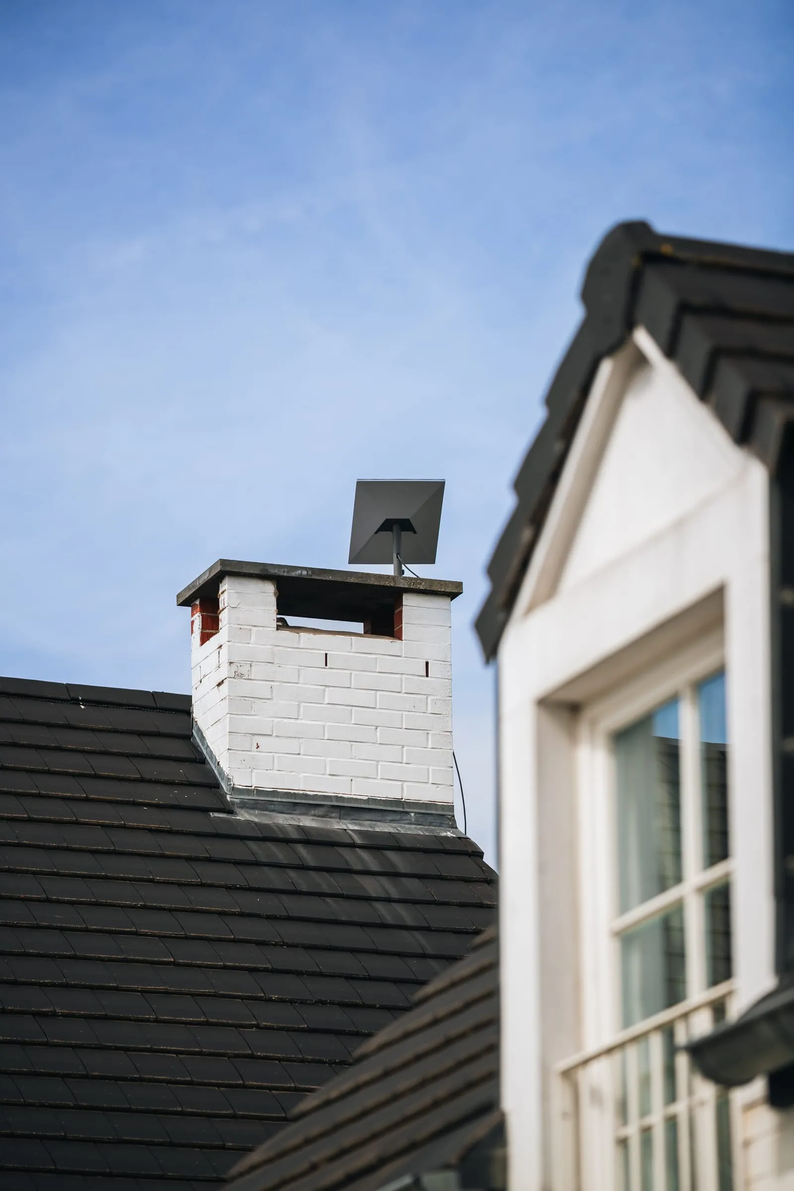 Antenne Starlink fixée sur une cheminée en brique blanche, ciel bleu