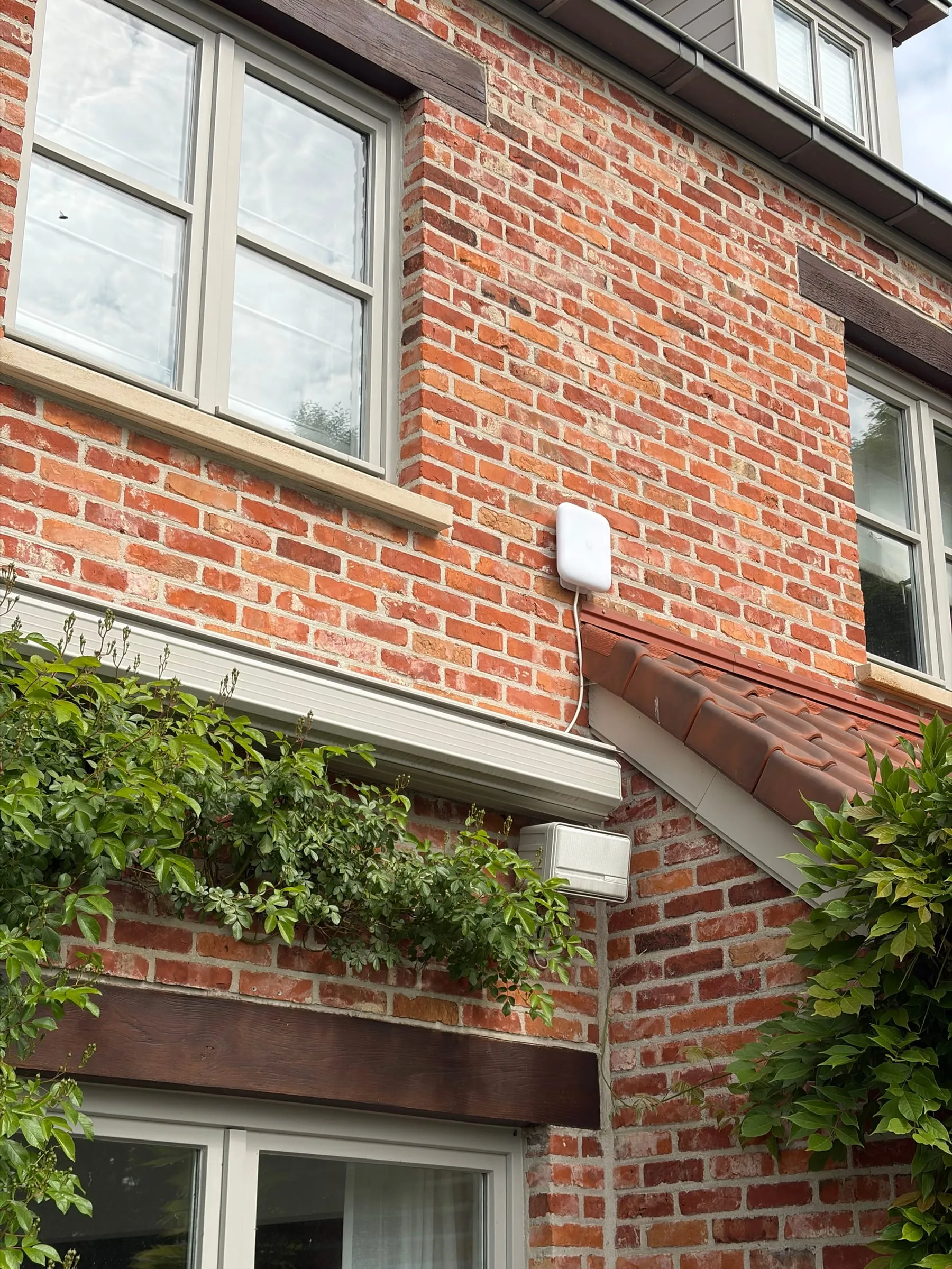 Borne Wi-Fi UniFi extérieure fixée sur la façade en brique d’une maison