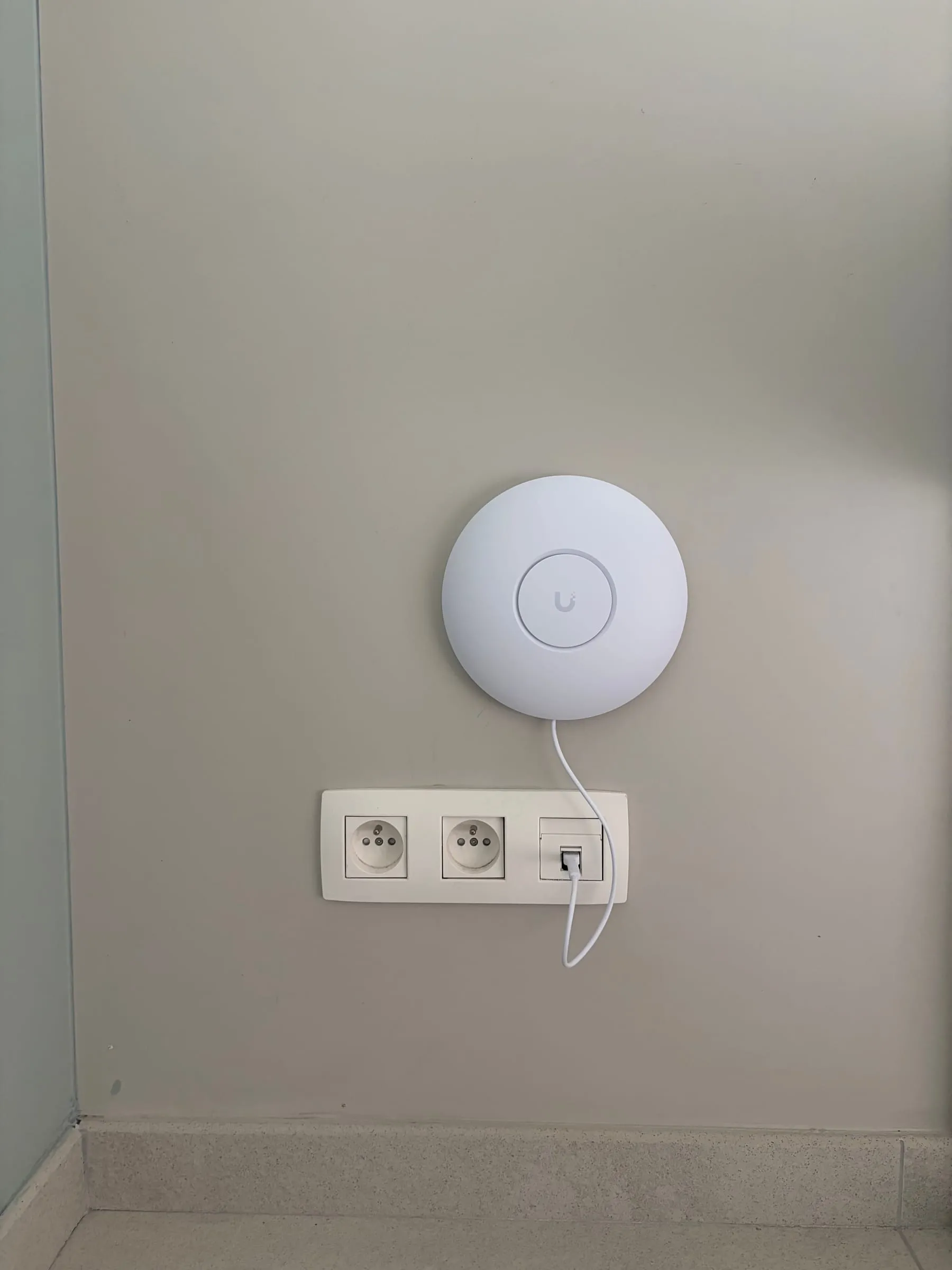 Borne Wi-Fi UniFi fixée au mur, reliée à une prise réseau