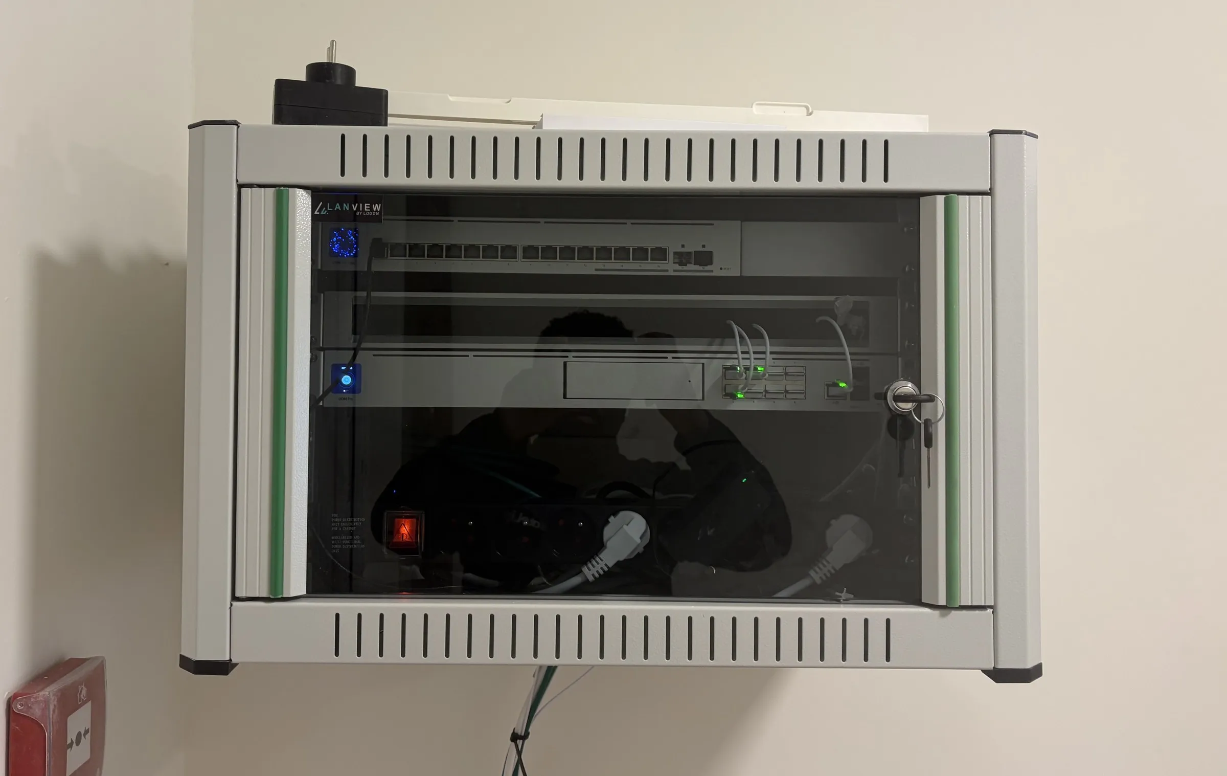 Baie réseau murale fermée à clé : un commutateur et la console UniFi visibles à travers la porte vitrée