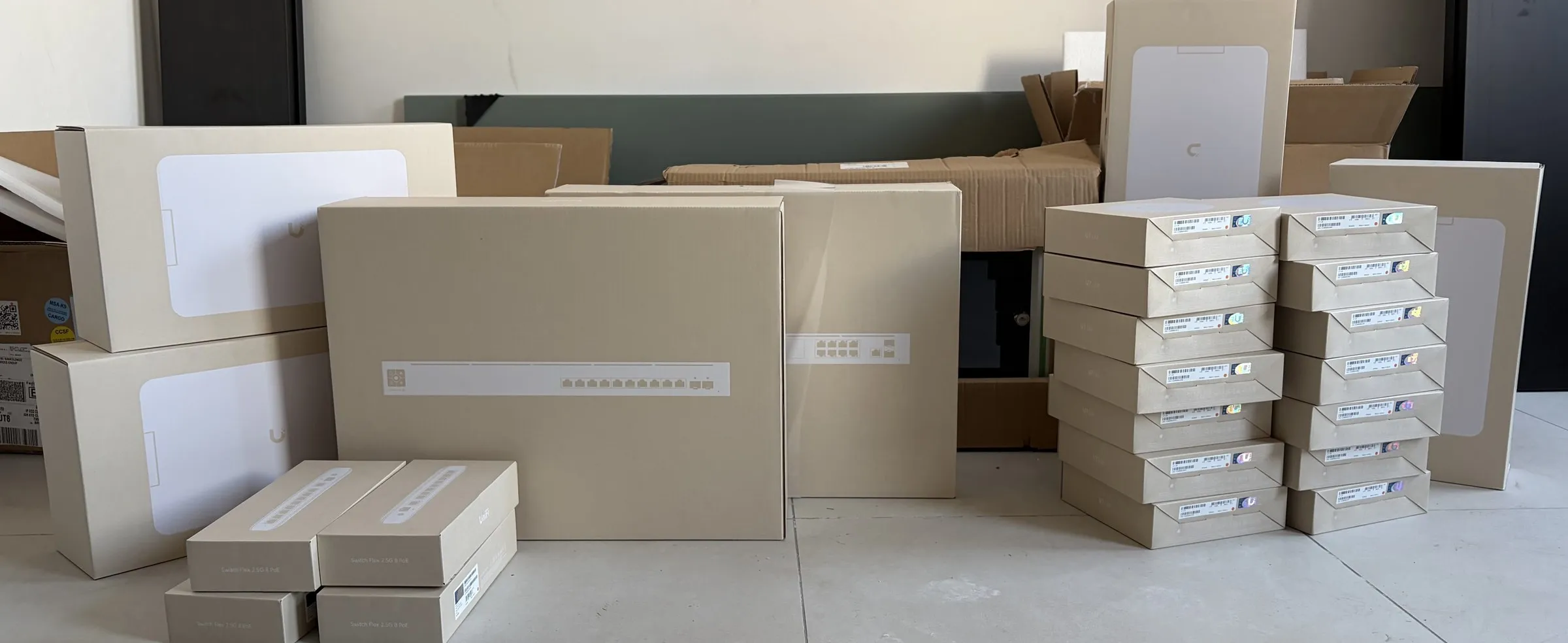 Cartons de matériel réseau empilés au sol d’une pièce vide : boîtes de bornes Wi-Fi et de commutateurs, avant la pose