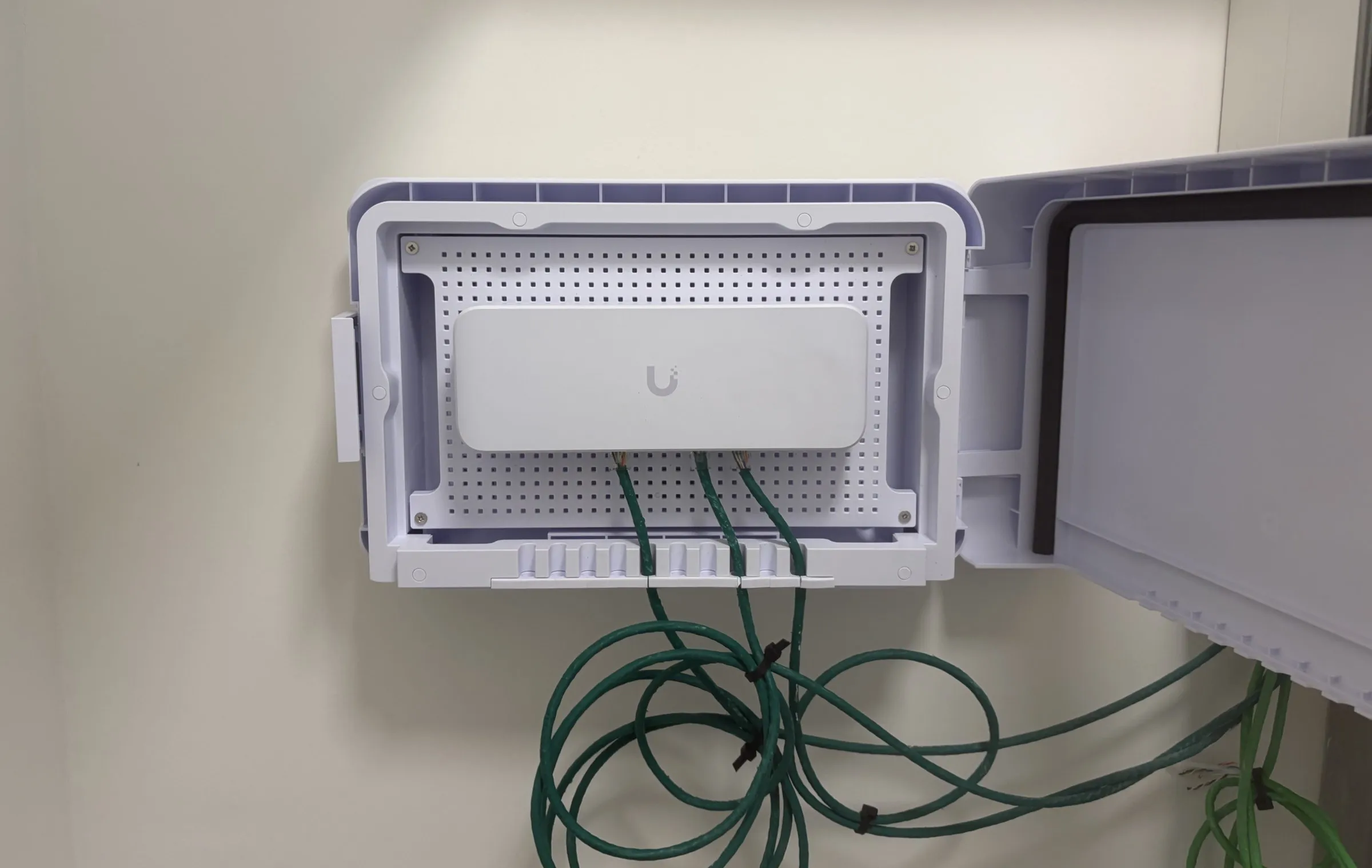 Boîtier mural ouvert d’un point de distribution UniFi, avec trois câbles réseau verts raccordés