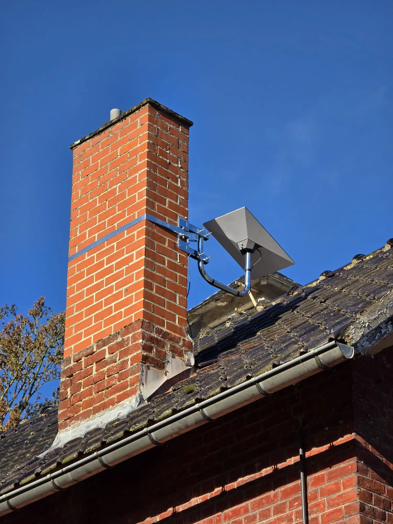 Antenne Starlink fixée à une cheminée en brique rouge, sur le toit d'une maison