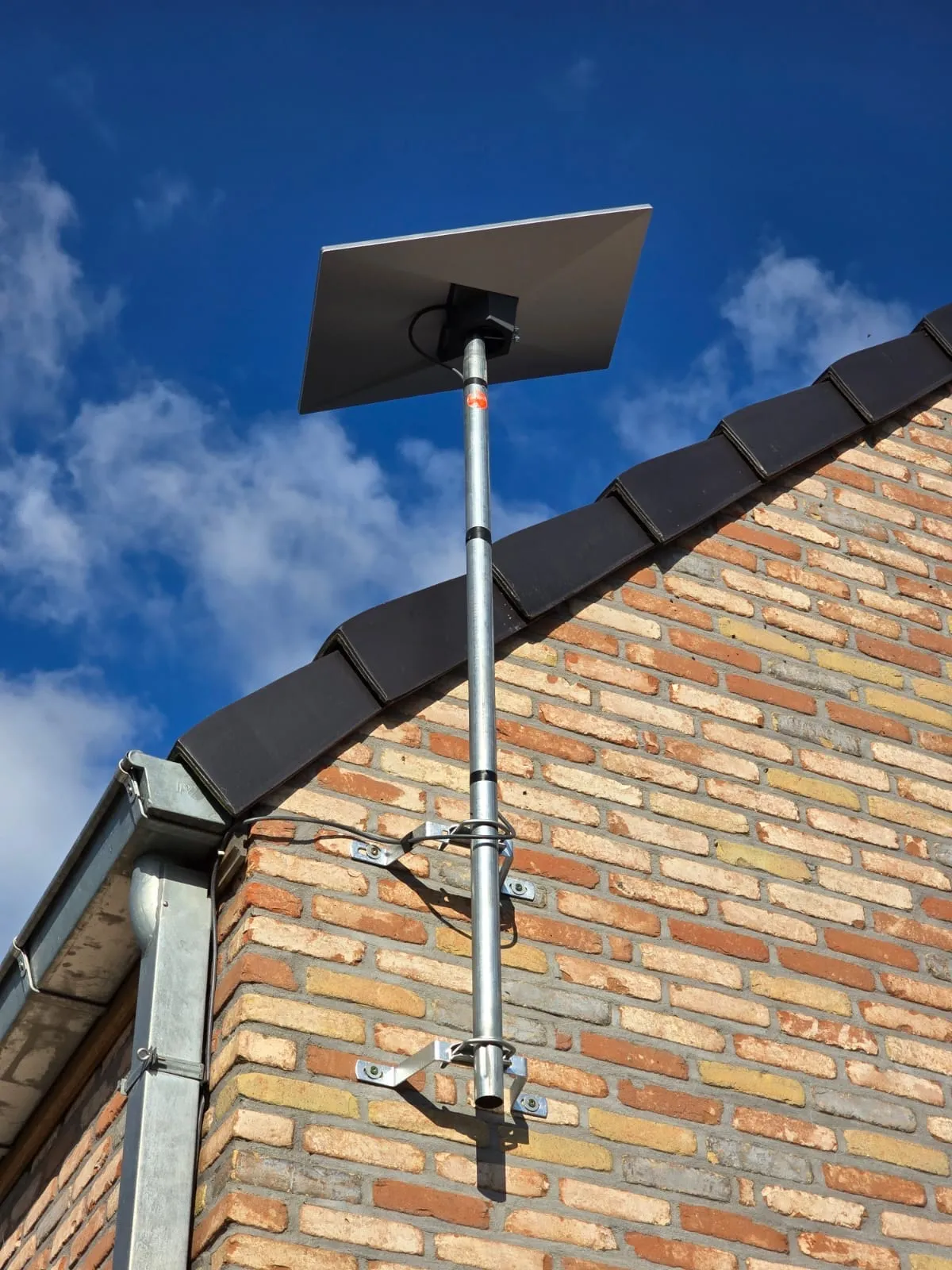 Antenne Starlink sur un mât fixé au pignon en brique d'une maison