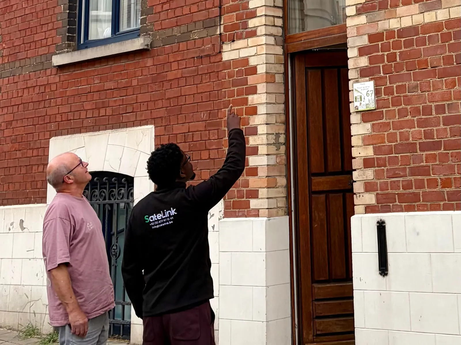 Romuald, en tenue SateLink, montre à un client un point sur la façade de sa maison